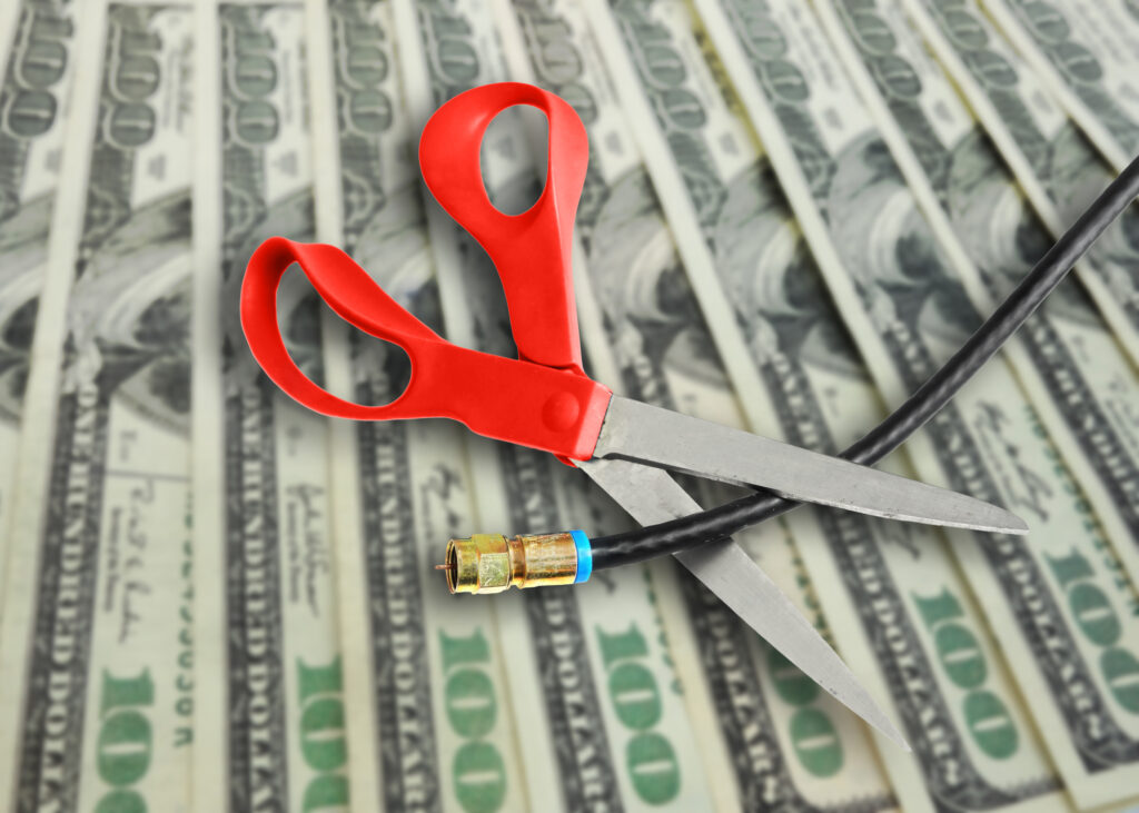 Scissors cutting a coax cable on cash background -- cutting the cord to save money concept