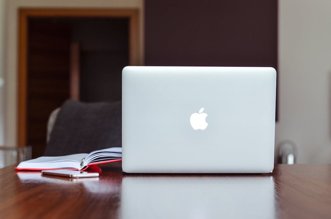 an open macbook setting on a desk next to an open book