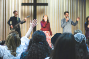 Audience member raises a hand in a gesture of participation or agreement during an engaging presentation on Church Budgeting Templates, with speakers or performers blurred in the background on stage.