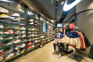 A shopper takes a break amidst a diverse collection of sneakers at a modern Nike Store, pondering their next purchase.