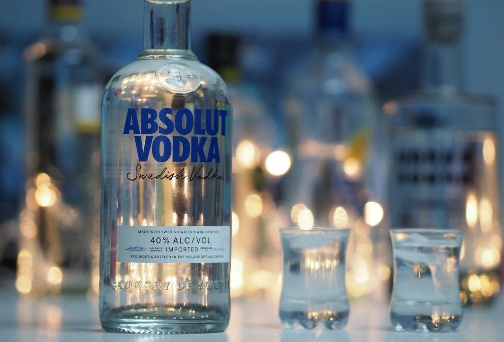 A clear bottle of absolut vodka with a blurred background showcasing lights and possibly other bottles, evoking a sophisticated, evening atmosphere. This setting not only highlights the beverage's elegance but subtly suggests various uses for
