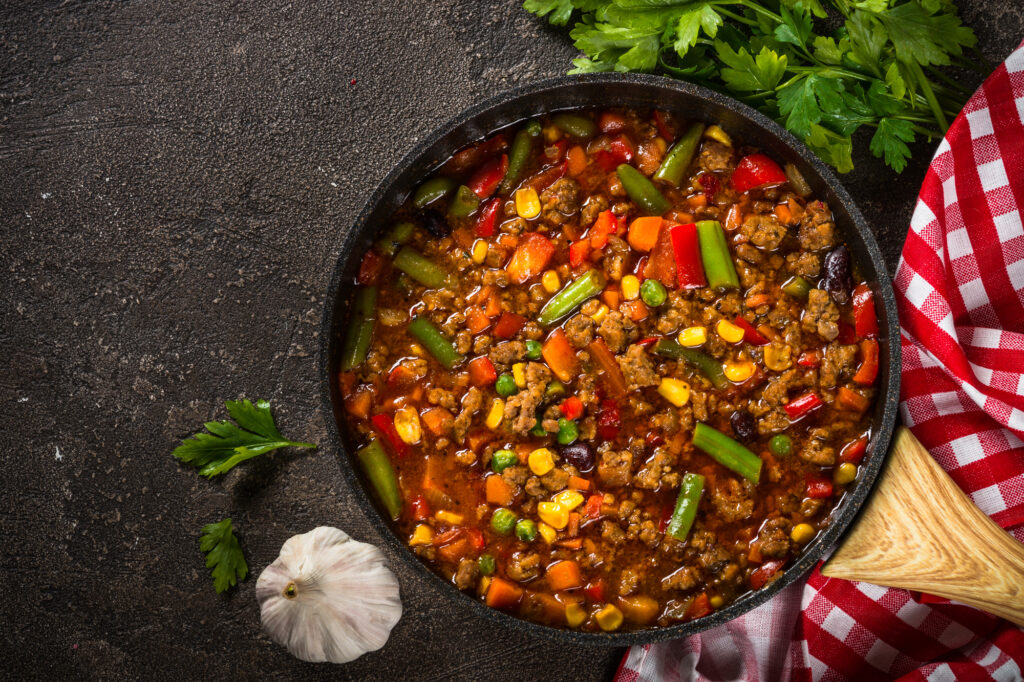 One-pot meals: Chili con carne in skillet on dark stone table.