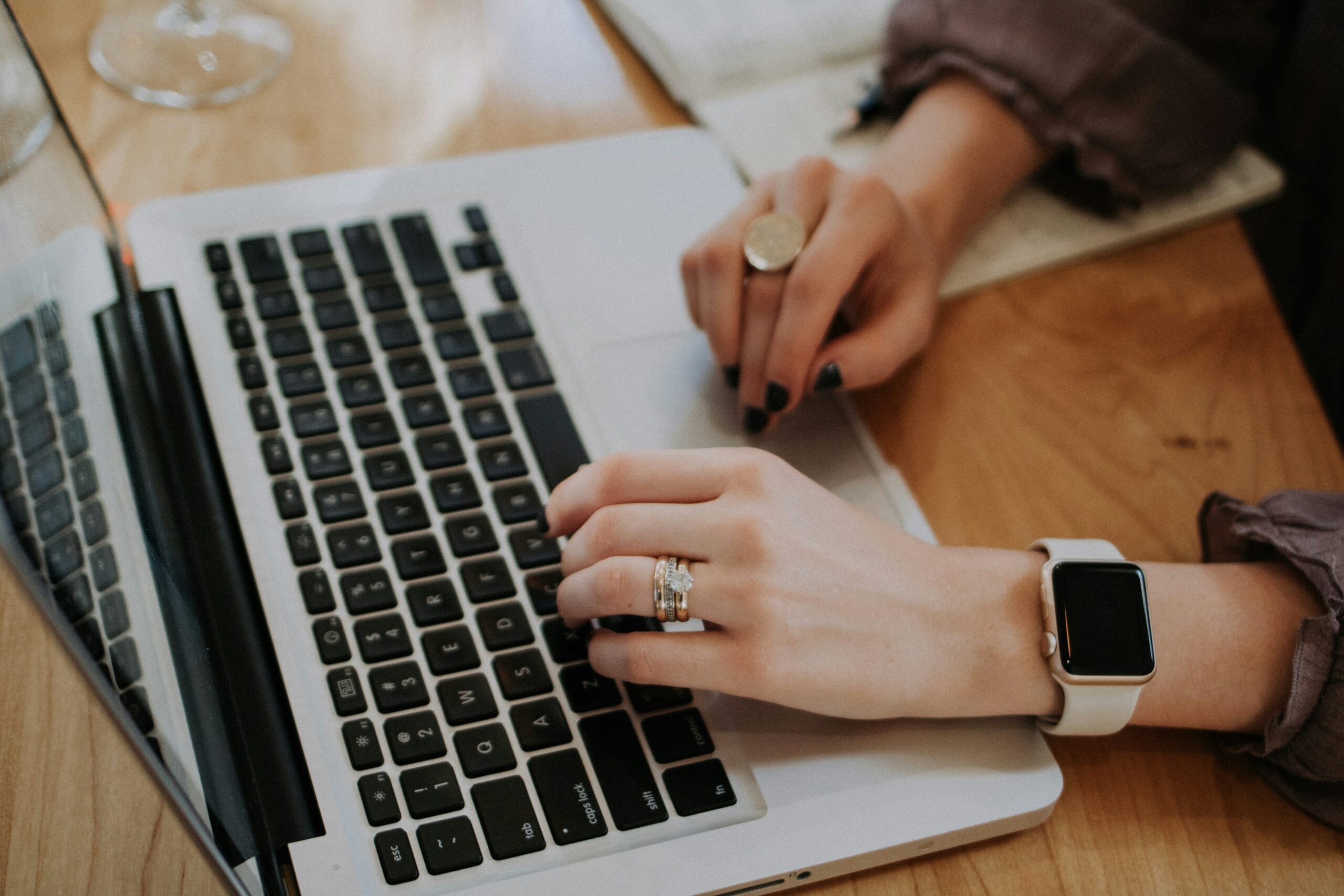 Close-up of a woman with two rings and a watch typing on her laptop. 