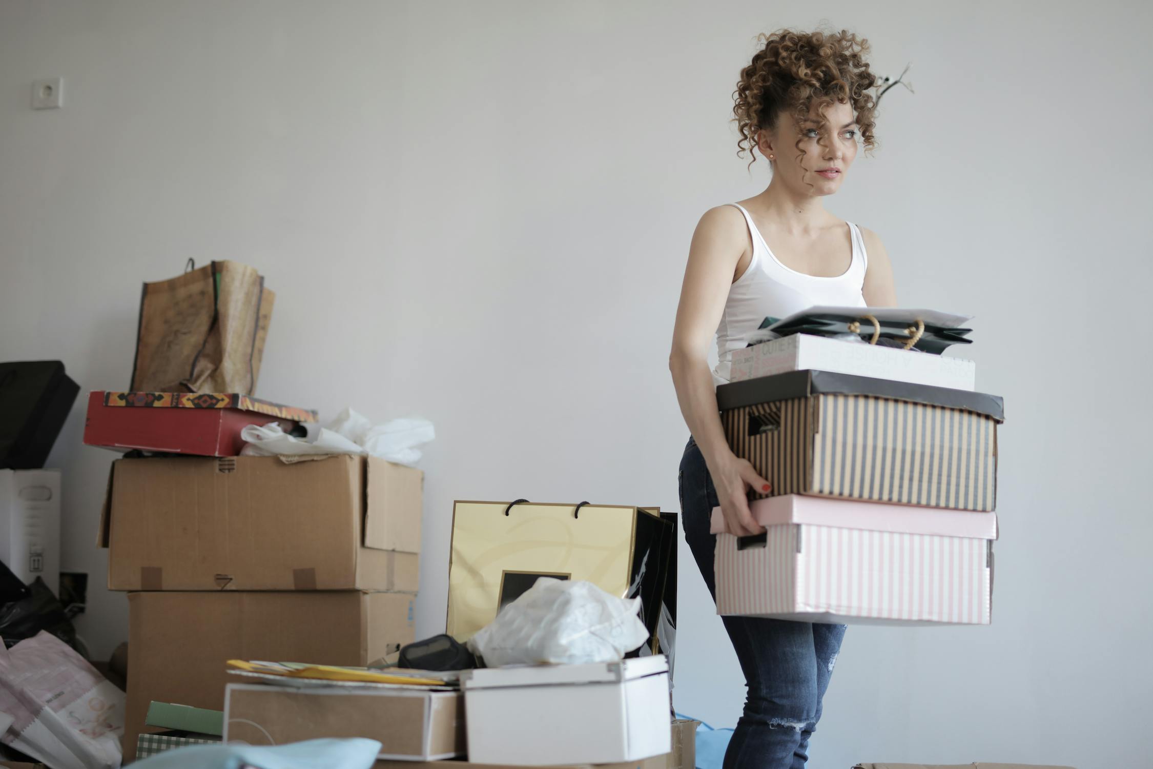 Girl holding stacked boxes and piles of clutter behind her. 