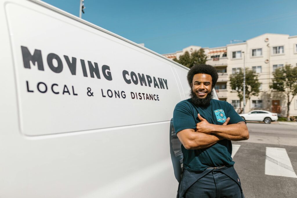 Man in black pants and shirt leaning on a white moving van.