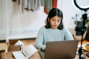 Hispanic lady working remotely on laptop near notebook in room