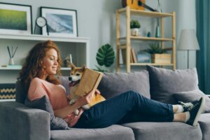 lady reading a book on the couch with a dog while on a staycation