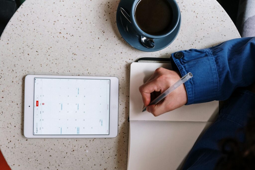 A person with a notepad and a tablet with a calendar in front of them.