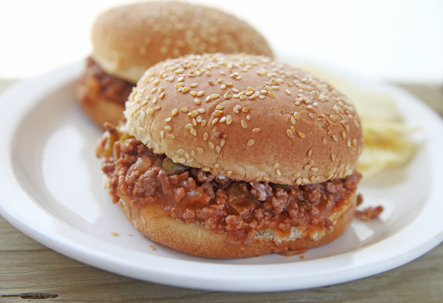 Two sloppy joe sandwiches on sesame seed buns with potato chips 