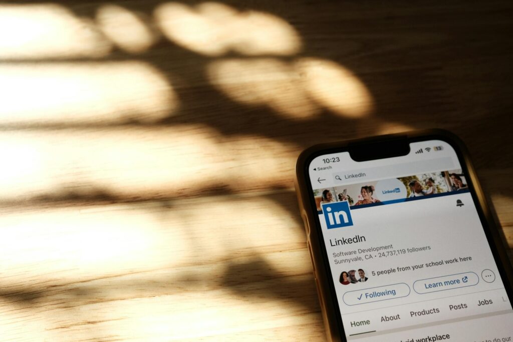 A smartphone displaying LinkedIn’s official page on its screen, placed on a wooden surface with soft natural light and shadows in the background.