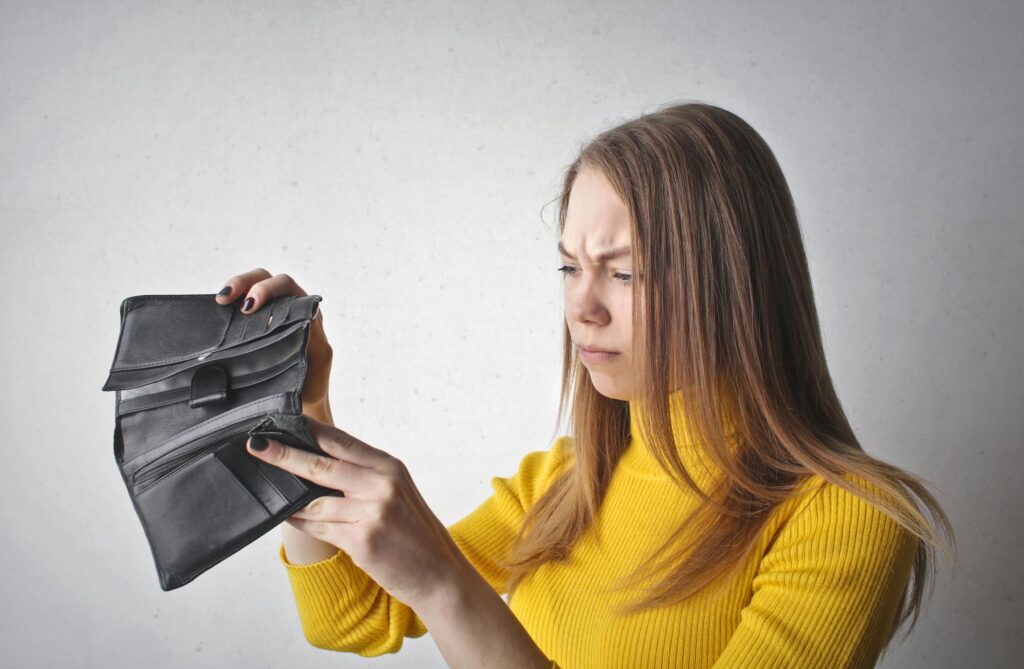 woman in yellow shirt looking through empty wallet