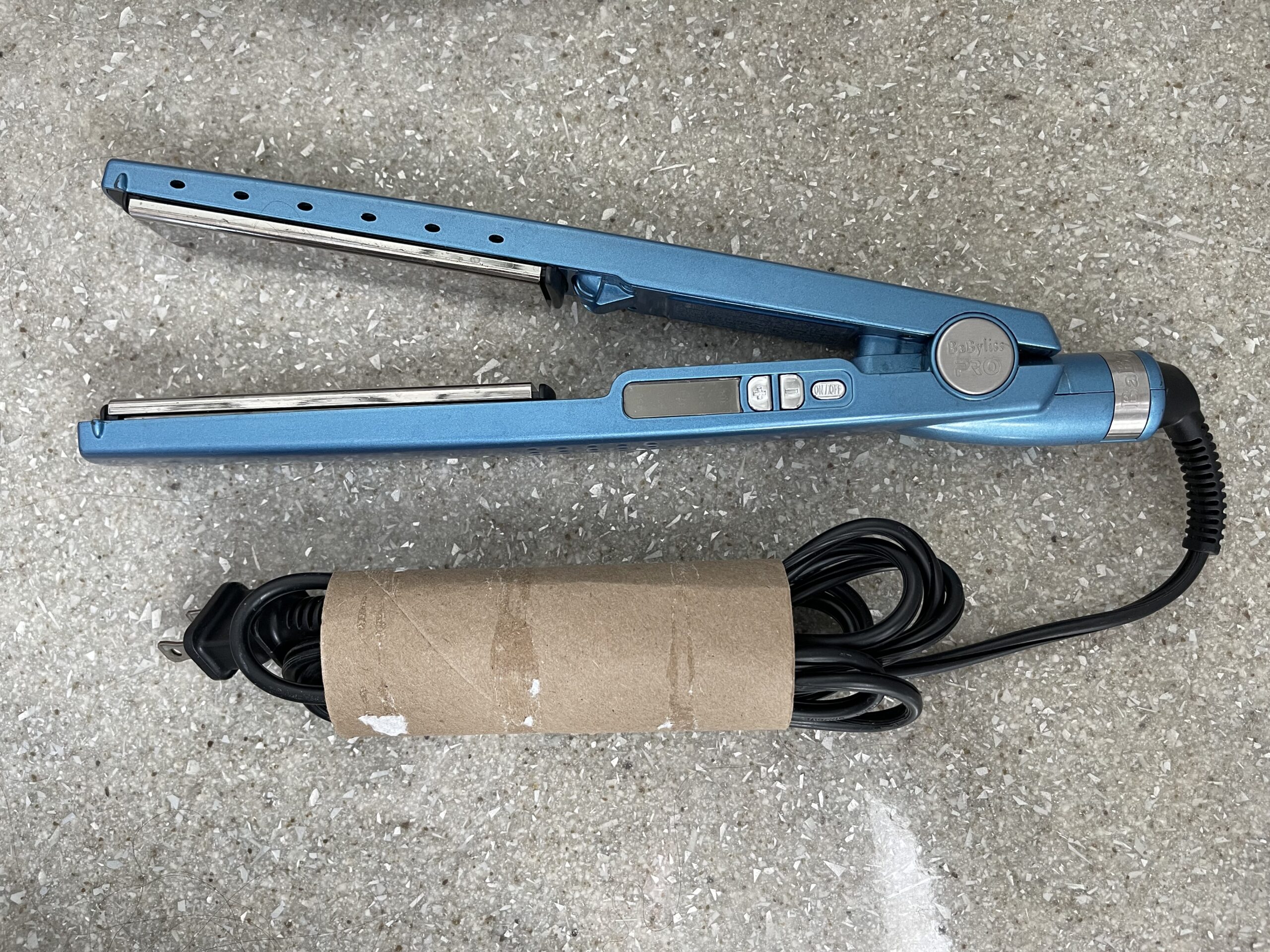 A blue BaBylissPRO hair straightener with its power cord neatly wrapped and secured inside a repurposed cardboard tube.