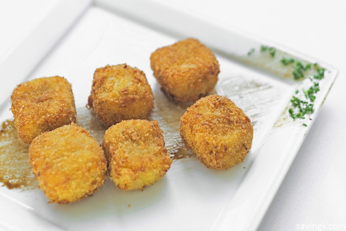 Golden, crispy mashed potato croquettes served on a white plate with a garnish of fresh herbs.