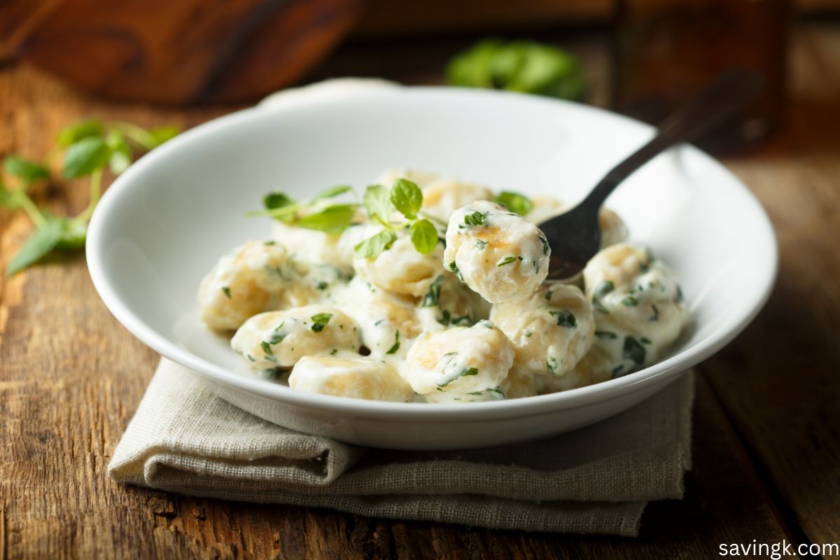 A bowl of homemade potato gnocchi in a creamy herb sauce, garnished with fresh basil, served on a rustic wooden table.