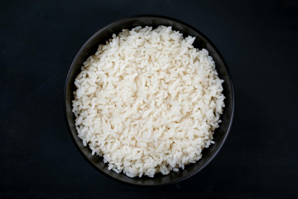 A black bowl filled with cooked white rice on a dark background.