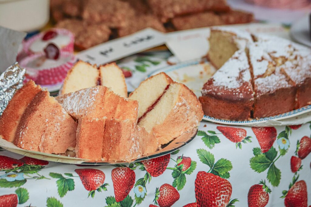 A close-up of sliced pound cake with a dusting of powdered sugar, arranged on plates over a strawberry-patterned tablecloth.