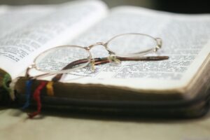 A pair of reading glasses resting on an open Bible, with colorful ribbon bookmarks visible on the edge of the pages.