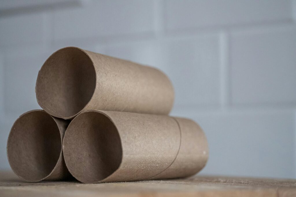 A close-up of three stacked empty cardboard tubes from toilet paper rolls, placed on a wooden surface against a neutral background.