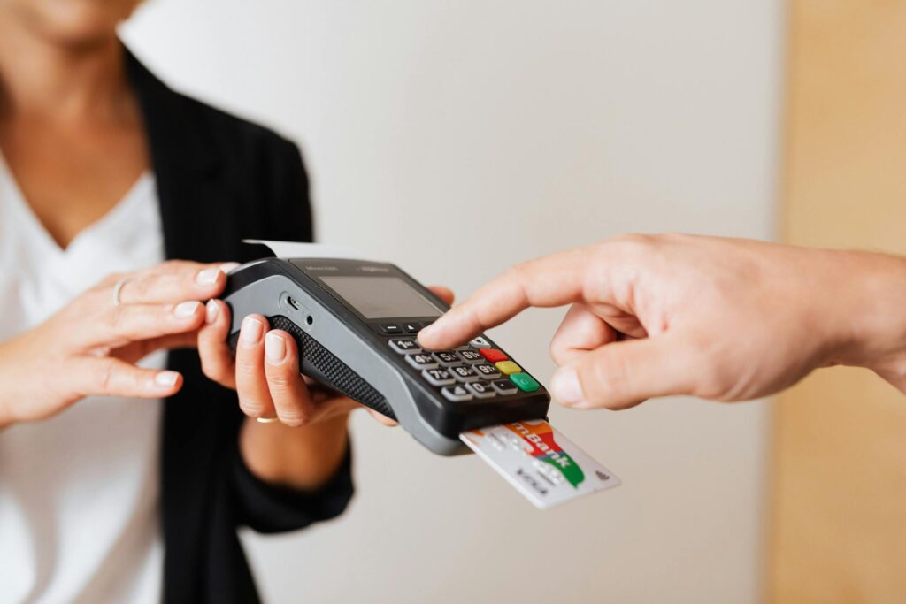 A close-up of a person making a payment using a credit card on a portable card reader held by a business employee.