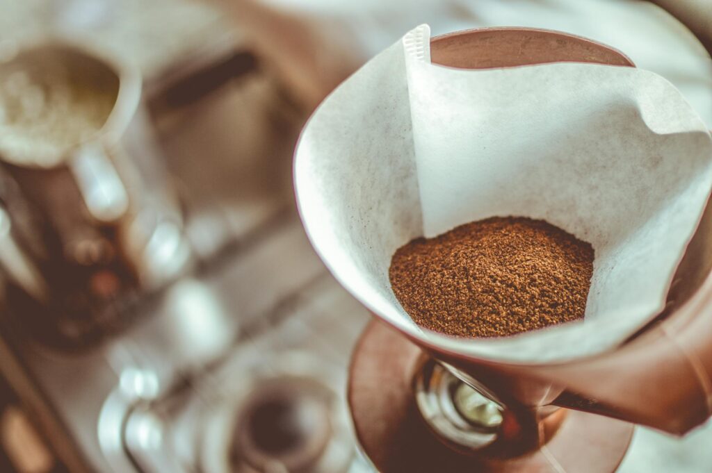 A close-up shot of a pour-over coffee filter filled with freshly ground coffee, with a blurred kitchen background.