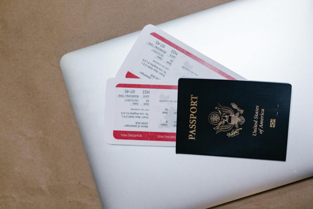 A U.S. passport placed on top of a silver laptop, with two boarding passes partially tucked underneath.