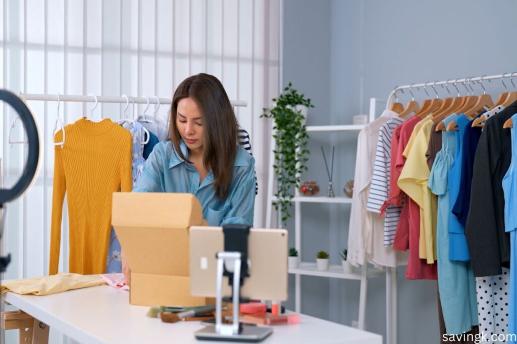 A young woman packing a shipping box in a home-based workspace, surrounded by clothing racks and beauty products, preparing an online sale for Mercari.