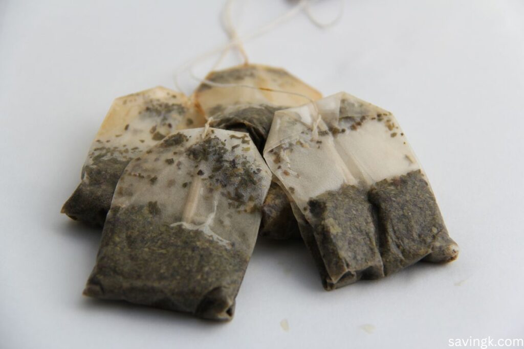 A close-up of several used tea bags placed on a white surface, showing the damp tea leaves inside the porous bags.