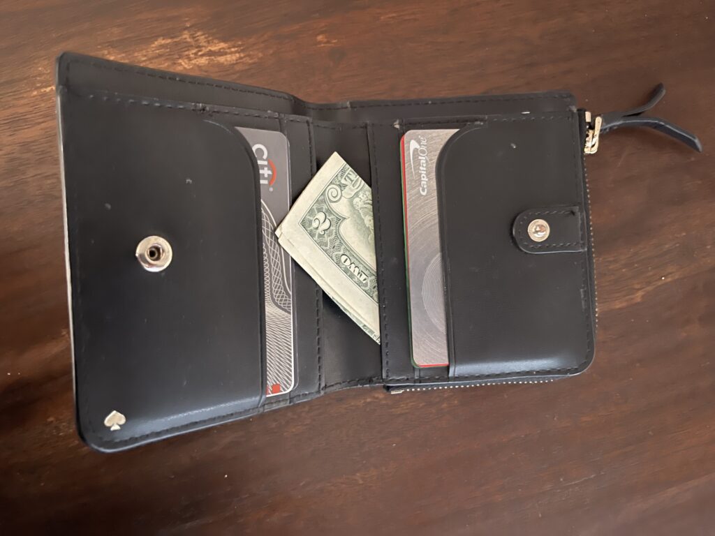 A black wallet opened on a wooden surface, revealing a folded $2 bill tucked between credit cards.