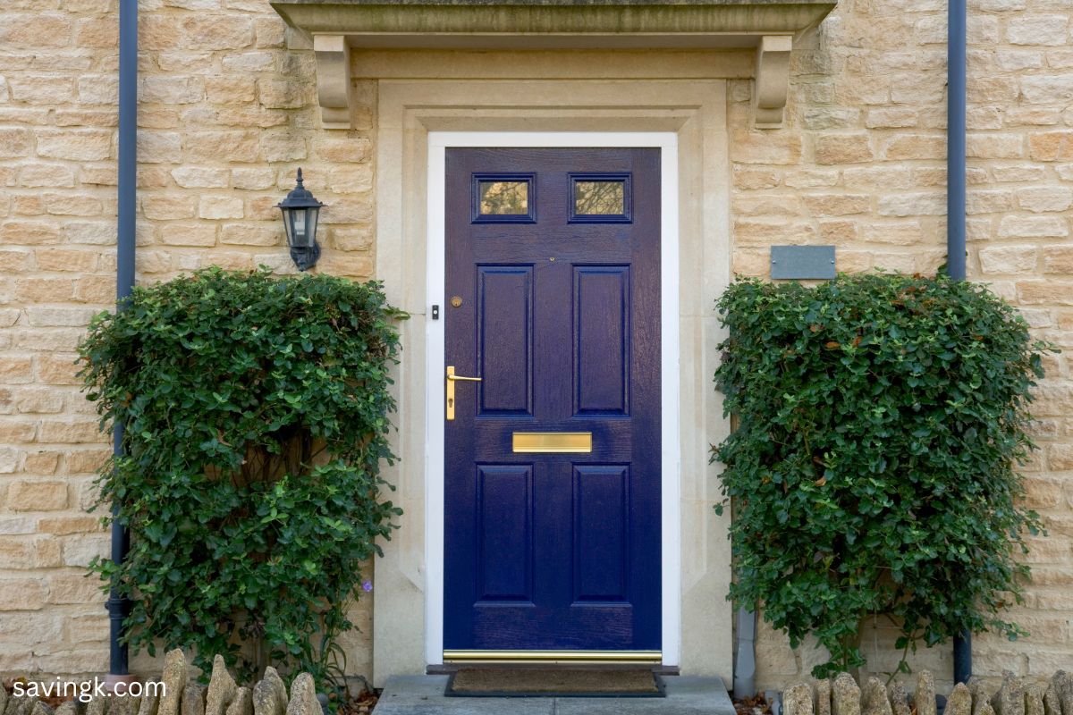 A deep blue front door with gold hardware, framed by lush greenery and set against a stone facade. In Feng Shui, a blue door symbolizes money flow, opportunities, and abundance.