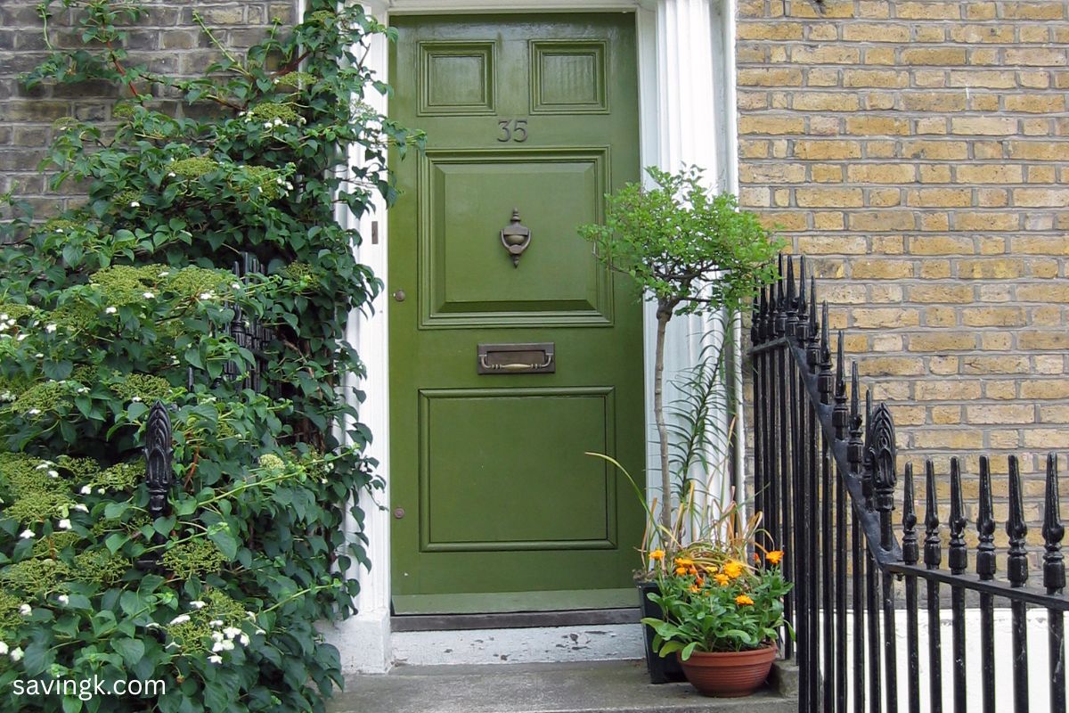 A classic green front door with brass hardware, framed by lush greenery and potted plants. In Feng Shui, a green door symbolizes financial growth, stability, and prosperity.