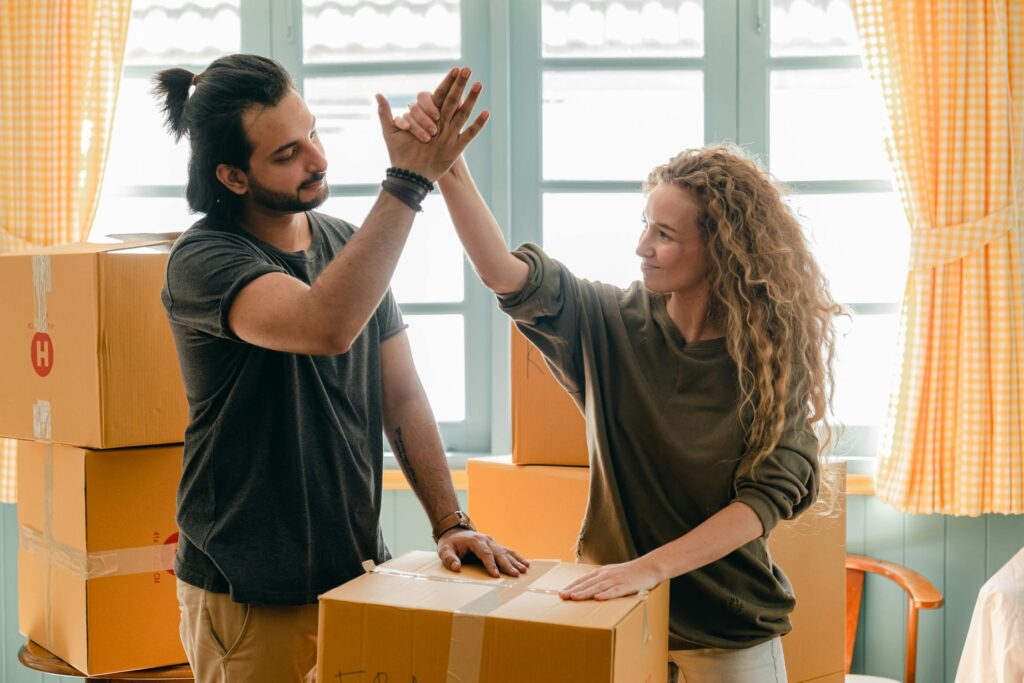 A couple high-fiving while unpacking boxes during a move, symbolizing the excitement and teamwork involved when moving for love