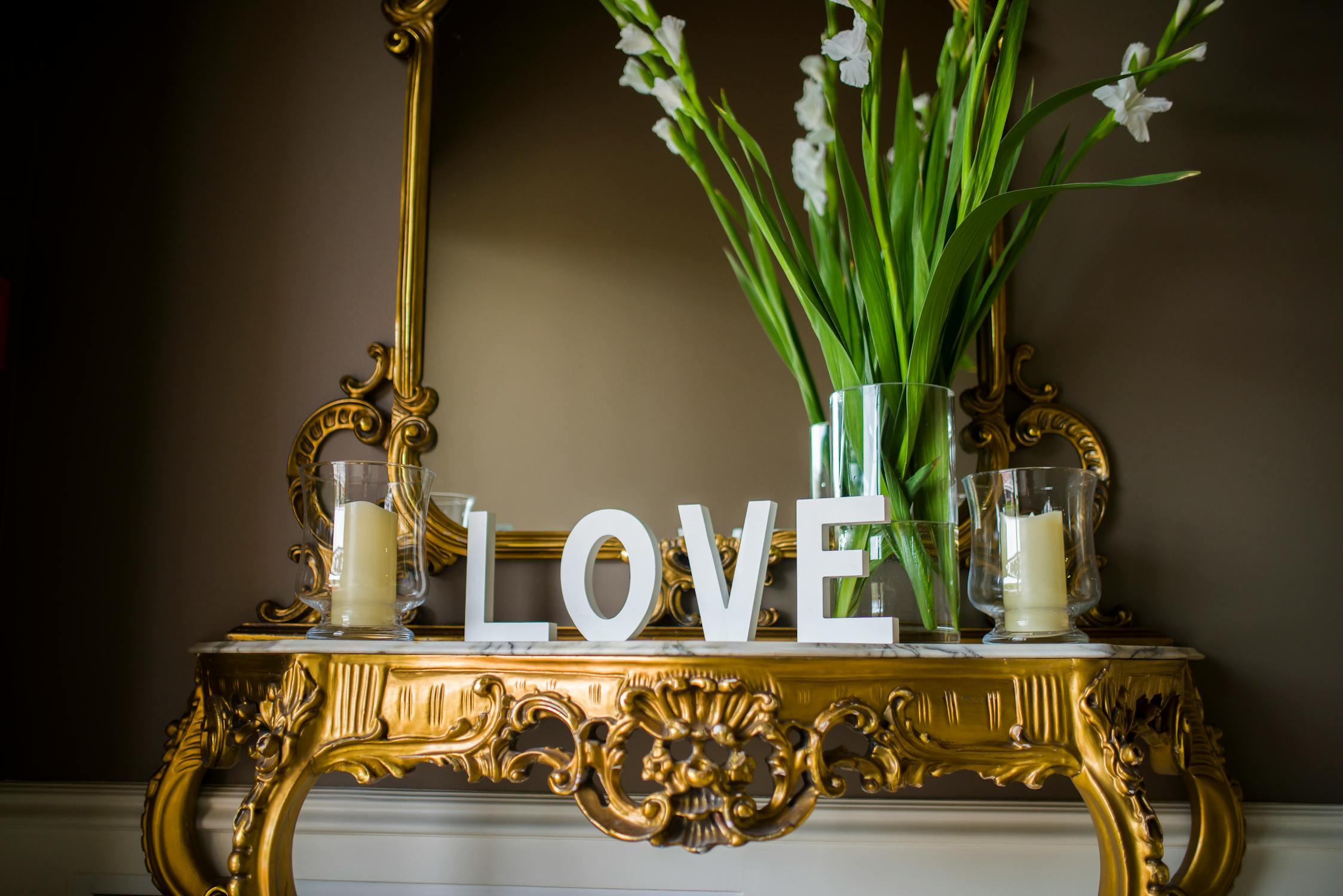 Elegant gold console table with a decorative mirror, white "LOVE" letters, and fresh flowers, symbolizing wealth and harmony.