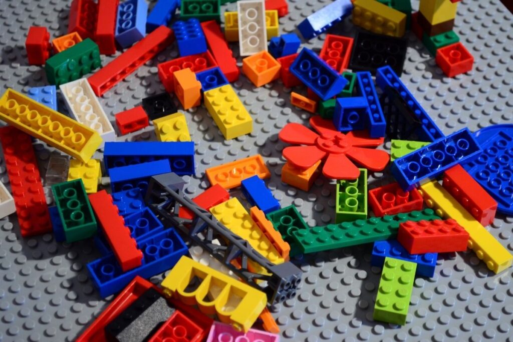Colorful LEGO bricks scattered on a gray baseplate, including red, blue, yellow, green, and orange pieces.