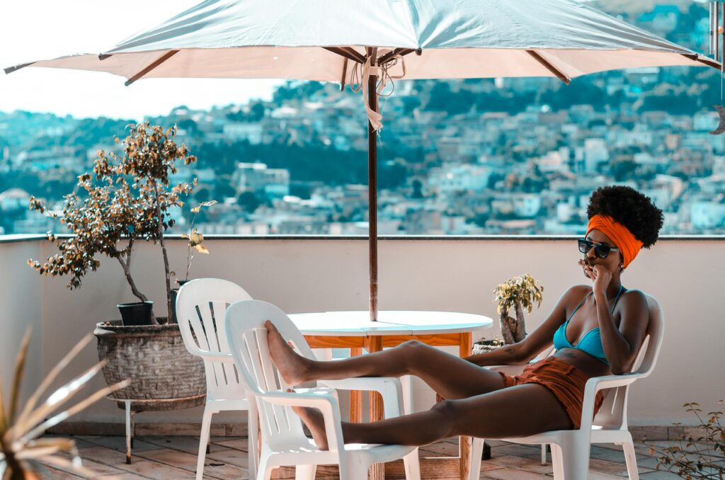 Woman relaxing on a rooftop patio under a sun umbrella with a scenic city view in the background.
