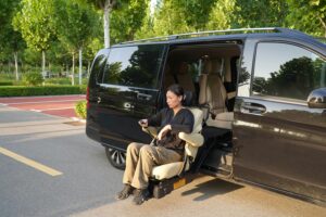 Woman using a mobility-accessible vehicle seat lift outside a black van in a sunny parking lot.