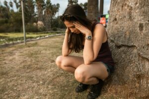Woman sitting outdoors with her head in her hands, showing signs of stress or anxiety.