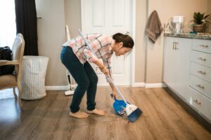 Woman sweeping up household clutter with a broom and dustpan in a clean, organized home.