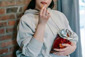 Woman in hoodie eating chips from a partially filled snack bag, illustrating the concept of shrinkflation.