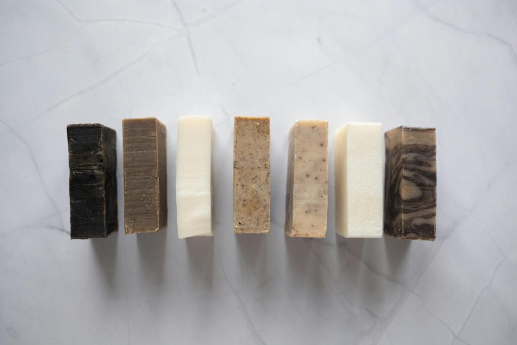 Handmade soap bars in various natural colors lined up on a white marble surface