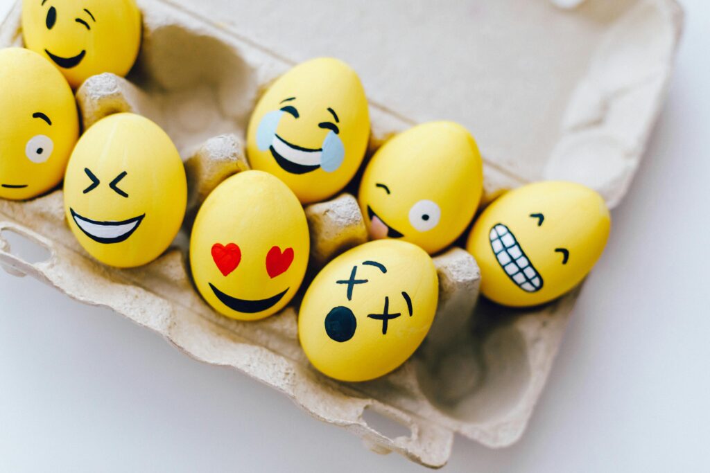 Yellow eggs decorated with fun emoji faces sitting in a cardboard egg carton.