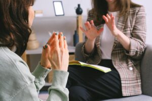 Two women in a counseling session, one taking notes while the other gestures with her hands, symbolizing a supportive and informative student loan counseling meeting.