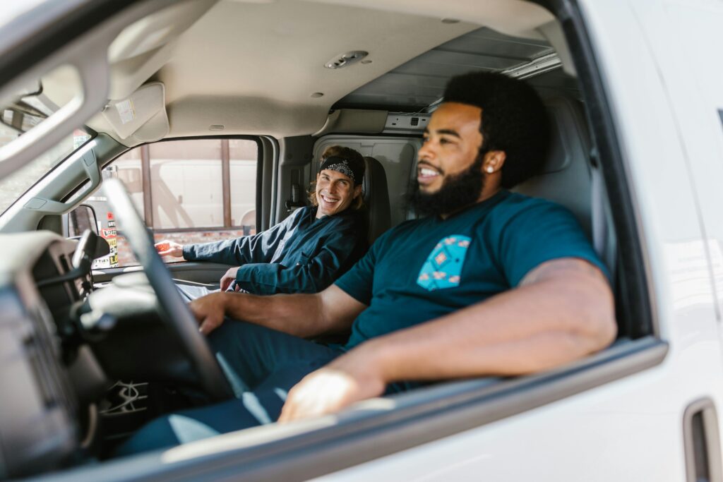 Two smiling men sit inside a van, possibly acquired through a government surplus program, highlighting community benefit and transportation access.