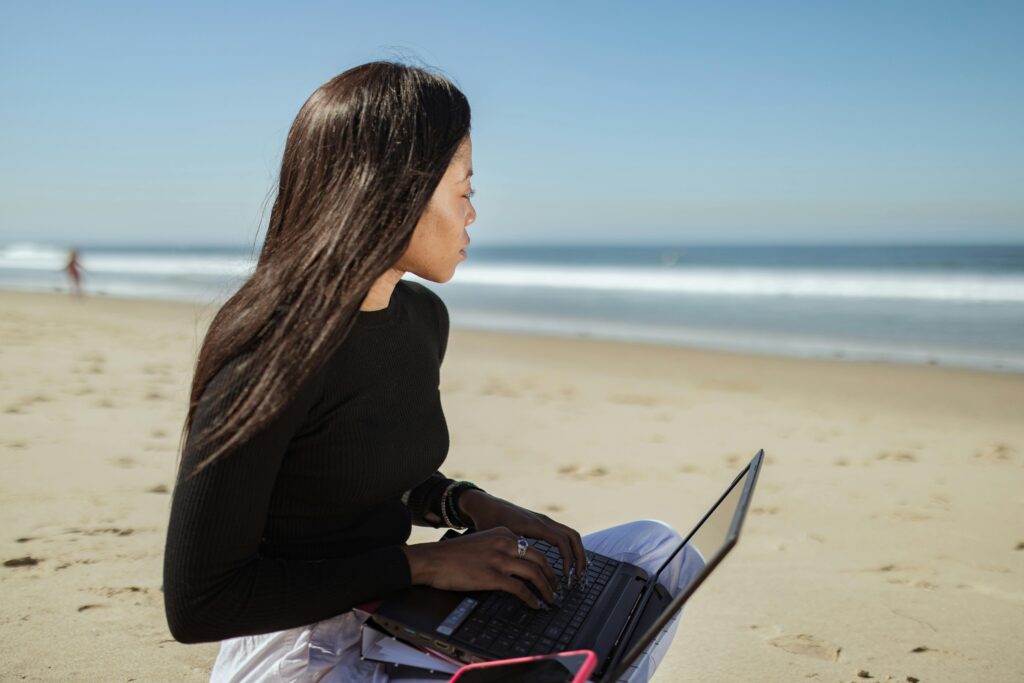 Woman working remotely on a laptop while sitting on a beach