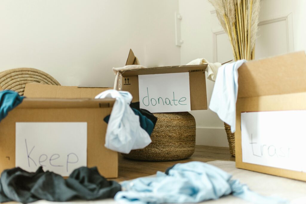 Labeled cardboard boxes marked "Keep," "Donate," and "Trash" filled with clothes during a home decluttering process.