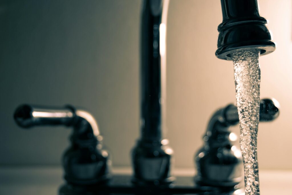 Close-up of a chrome bathroom faucet with running water, highlighting the importance of water conservation at home.