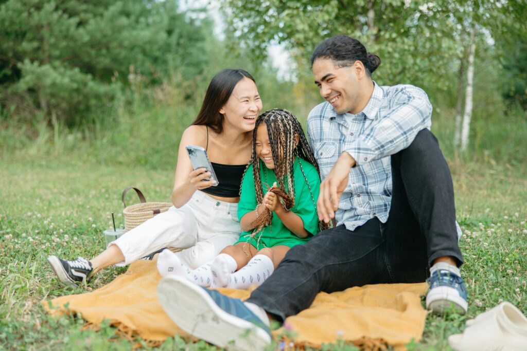 Smiling blended family sitting on a blanket outdoors, enjoying time together during a picnic.