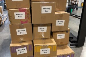 Stack of sealed cardboard mystery boxes labeled “Mystery Box” ready for sale in a warehouse setting.