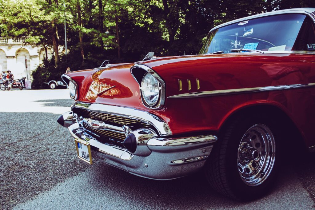 Close-up of a shiny red classic Chevrolet car with chrome details at an outdoor car show.