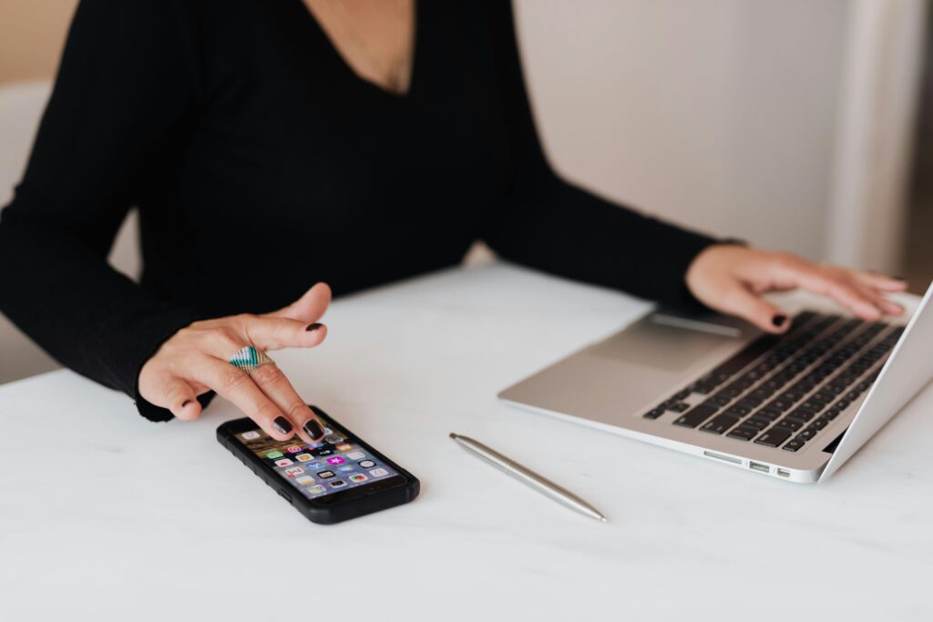 Person using a budgeting app on a smartphone while working on a laptop at a desk.
