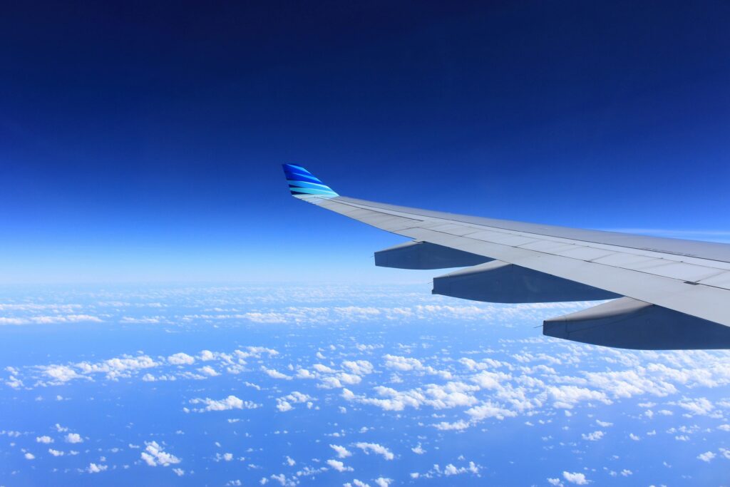 Airplane wing flying high above the clouds with a clear blue sky.